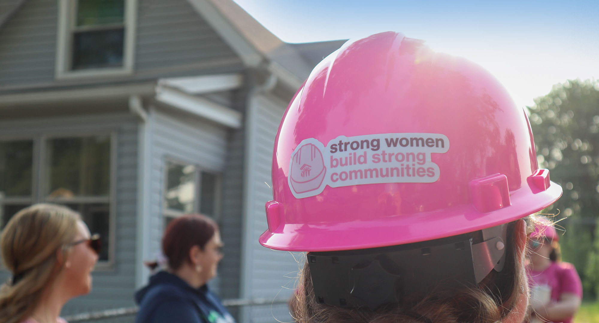 Pink hard hat with sticker "strong women build strong communities"