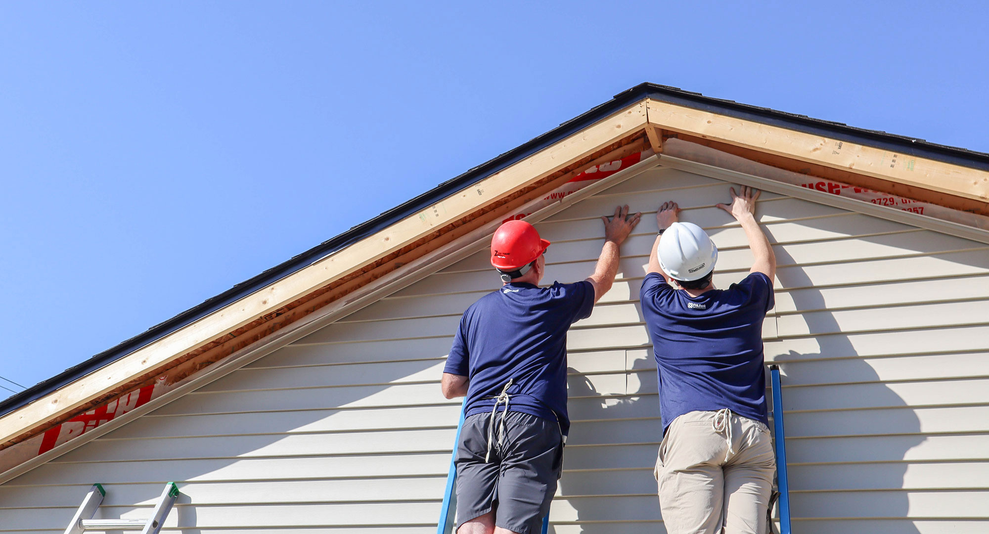 Two men on ladders installing siding on a home