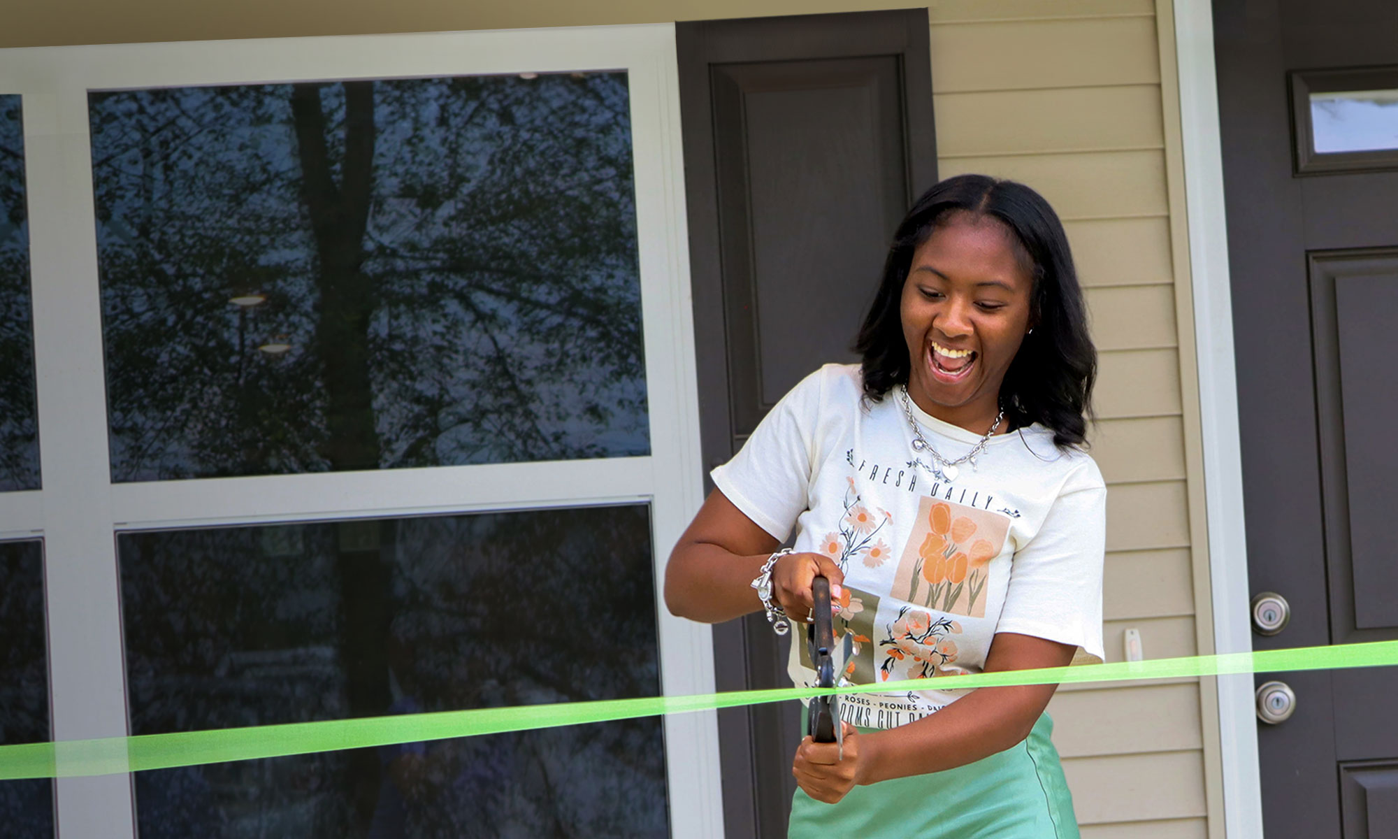 Young female cutting ribbon in front of new home